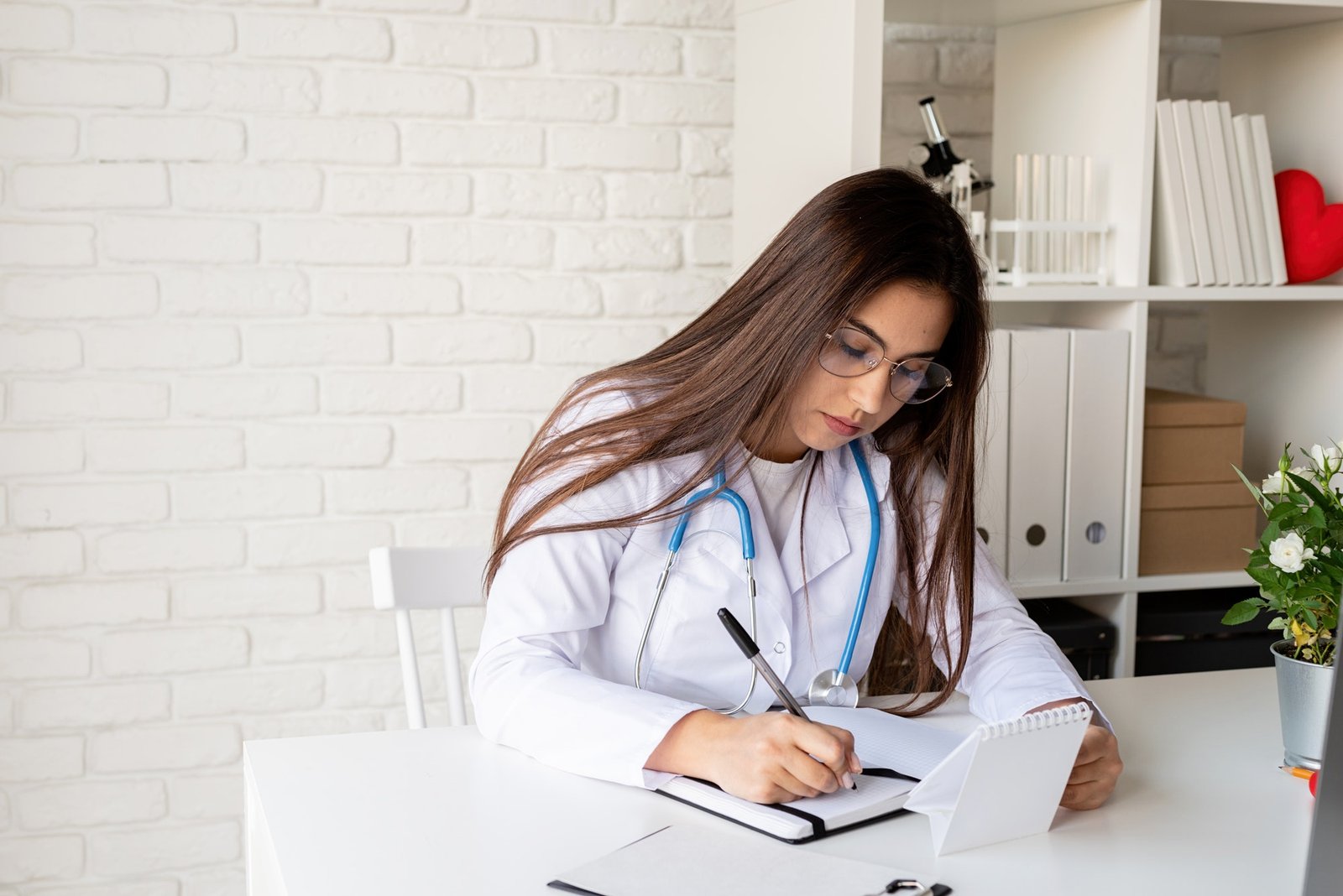 Young doctor woman writing in her cabinet filling medical history or anamnesis